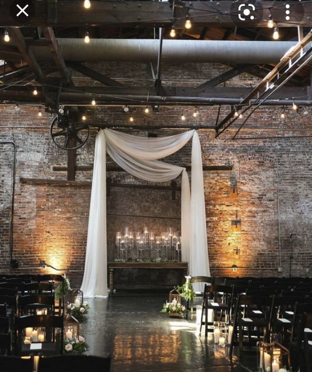 an indoor wedding venue with white draping and candles on the aisle, surrounded by brick walls