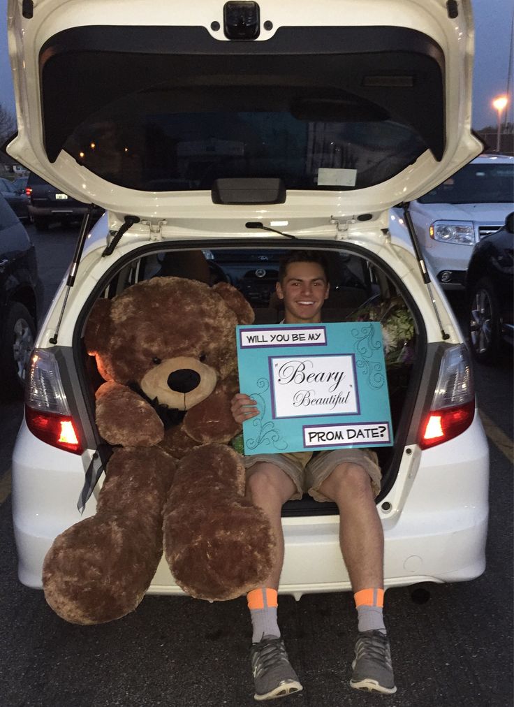 a man sitting in the back of a white car holding a large brown teddy bear