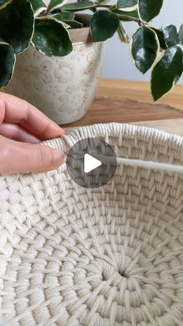 a person holding a knitting needle in front of a basket on a table with potted plants