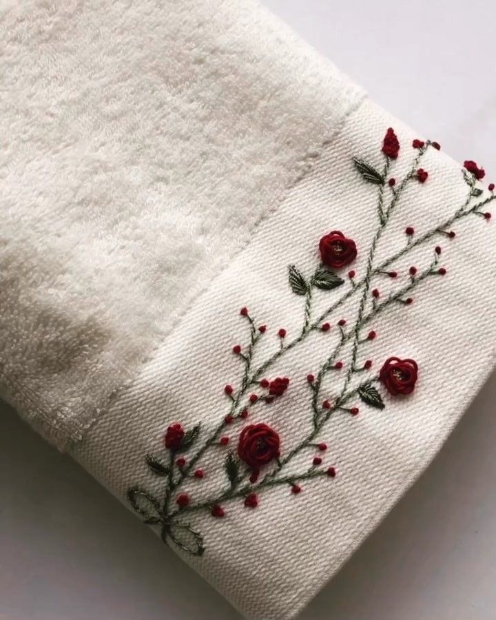 a white towel with red flowers embroidered on the front and side, sitting on top of a table