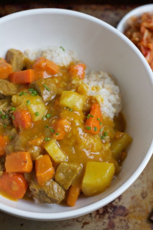 a white bowl filled with meat and vegetables on top of rice covered in gravy