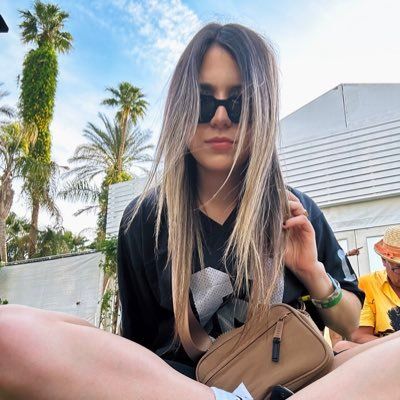 a woman sitting on the ground with her legs crossed, wearing sunglasses and holding a purse