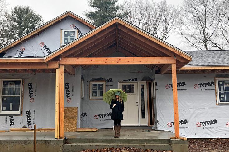 a woman holding an umbrella standing in front of a house under construction on a cloudy day