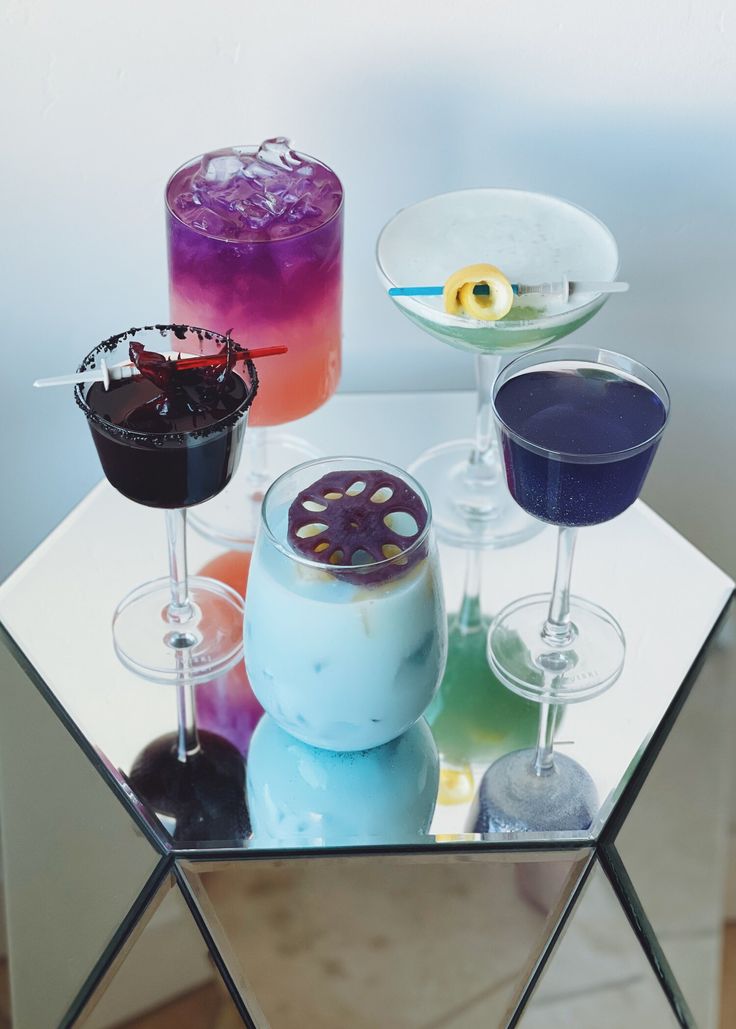 three different colored drinks sitting on top of a mirrored table next to each other in glasses