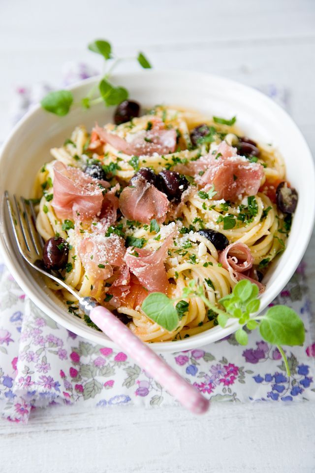 a white bowl filled with pasta and olives on top of a floral table cloth