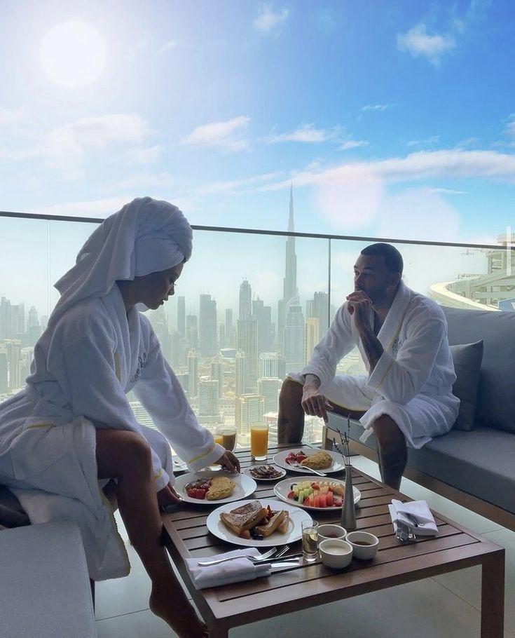 two people sitting at a table with plates of food in front of them, overlooking the city