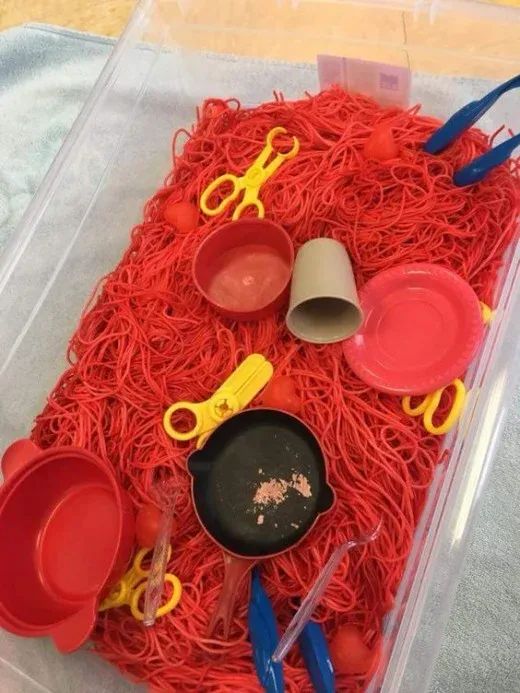 a plastic container filled with lots of red yarn next to scissors and other crafting supplies