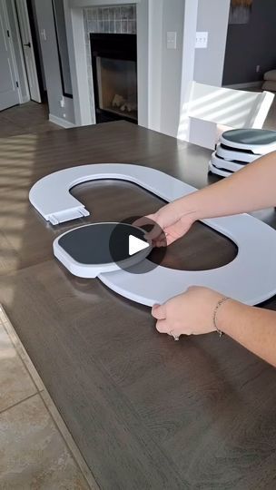 a woman is cutting out the letter g with scissors on a wooden table in front of a fireplace