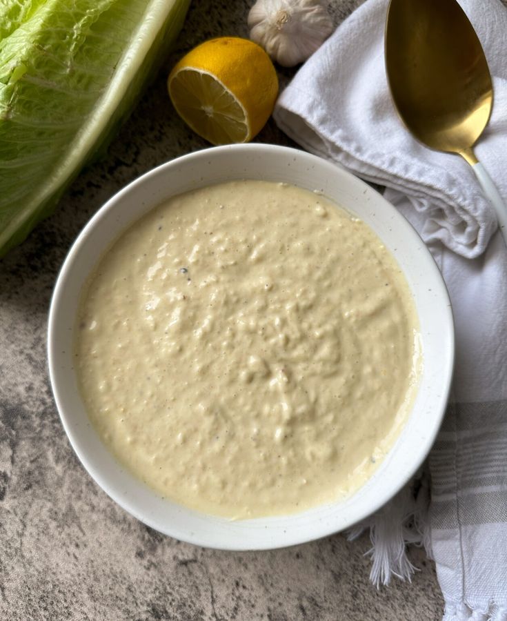 a white bowl filled with soup next to lettuce and lemons on a table