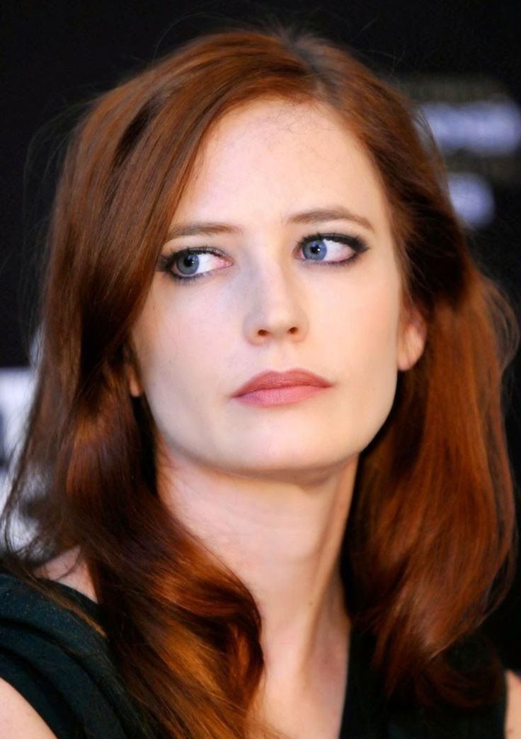 a woman with red hair and blue eyes looks at the camera while she is wearing black