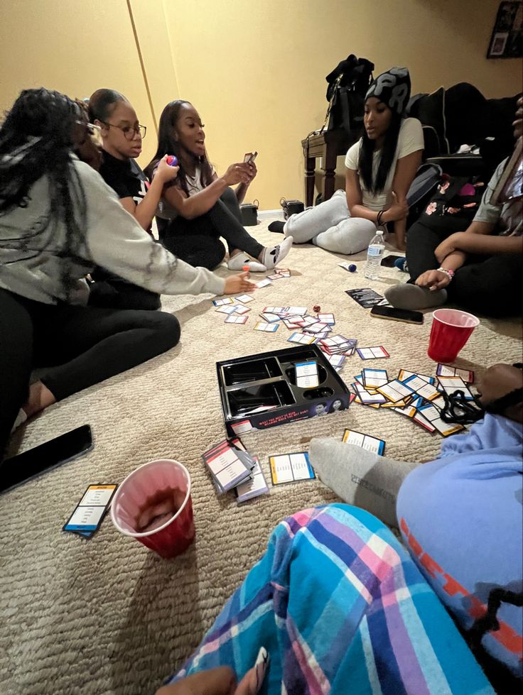 group of people sitting on the floor playing cards and drinking teas with their cell phones