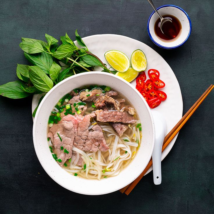 a white bowl filled with meat and noodles next to chopsticks