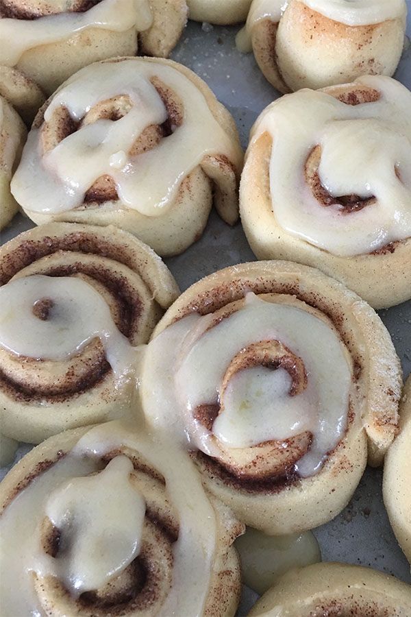 cinnamon rolls with icing sitting on top of a pan