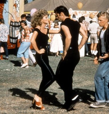 two men and a woman dancing in front of an amusement park with people watching them