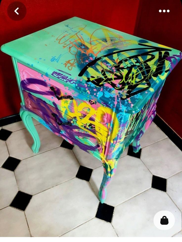 a colorful chest of drawers with graffiti painted on the top and bottom, sitting on a tiled floor