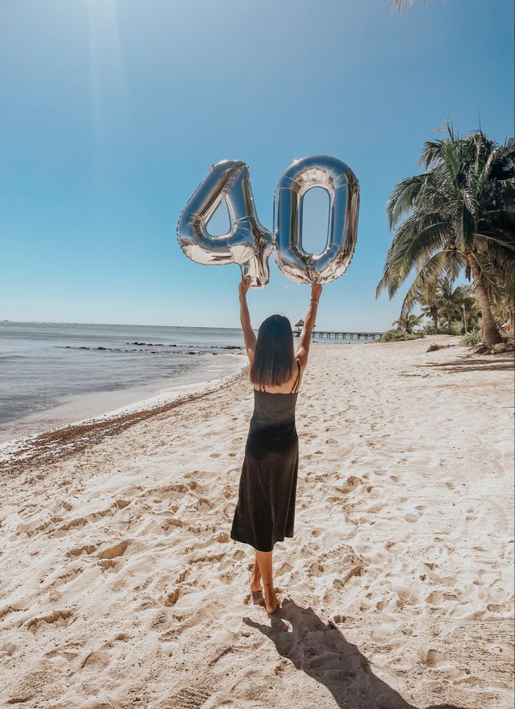 a woman on the beach holding up an inflatable number 40 balloon to the sky