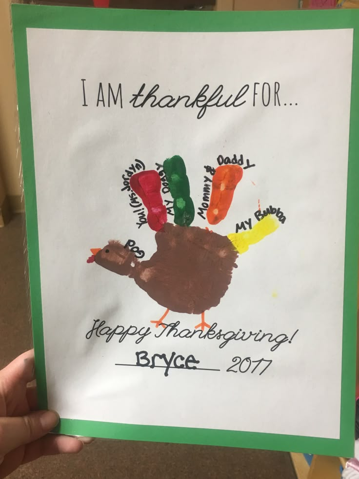 a child's hand holding up a card that says i am grateful for happy thanksgiving