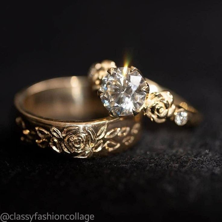 two gold wedding rings sitting on top of a black surface, with one diamond in the middle