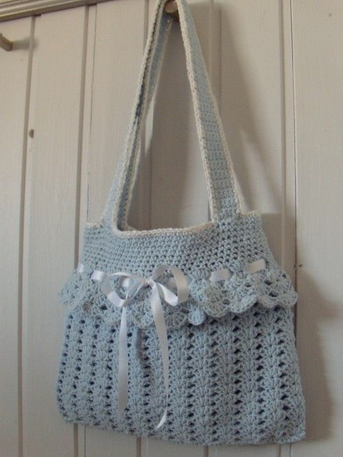 a crocheted purse hanging from a hook on a door handle with ribbon around it