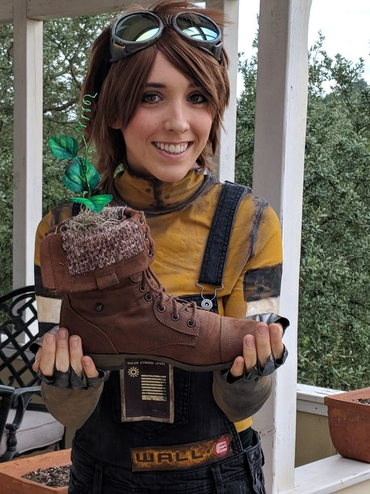 a woman wearing goggles and boots holds up a boot with a plant growing out of it