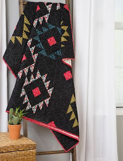 a black quilt hanging on the wall next to a potted plant