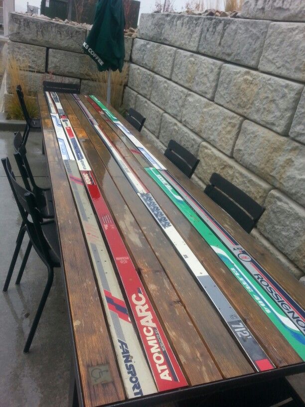 a wooden table with skis on it sitting in front of a stone wall and umbrella