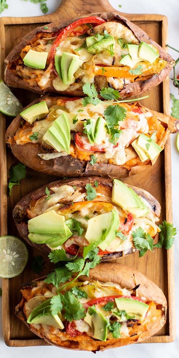 three loaded baked sweet potatoes with avocado, tomatoes and cilantro on a cutting board