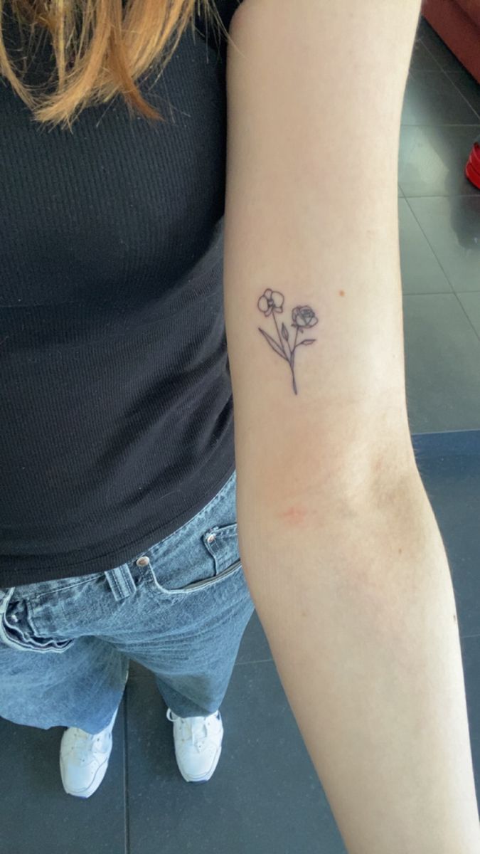 a woman's arm with a small flower tattoo on the left side of her arm