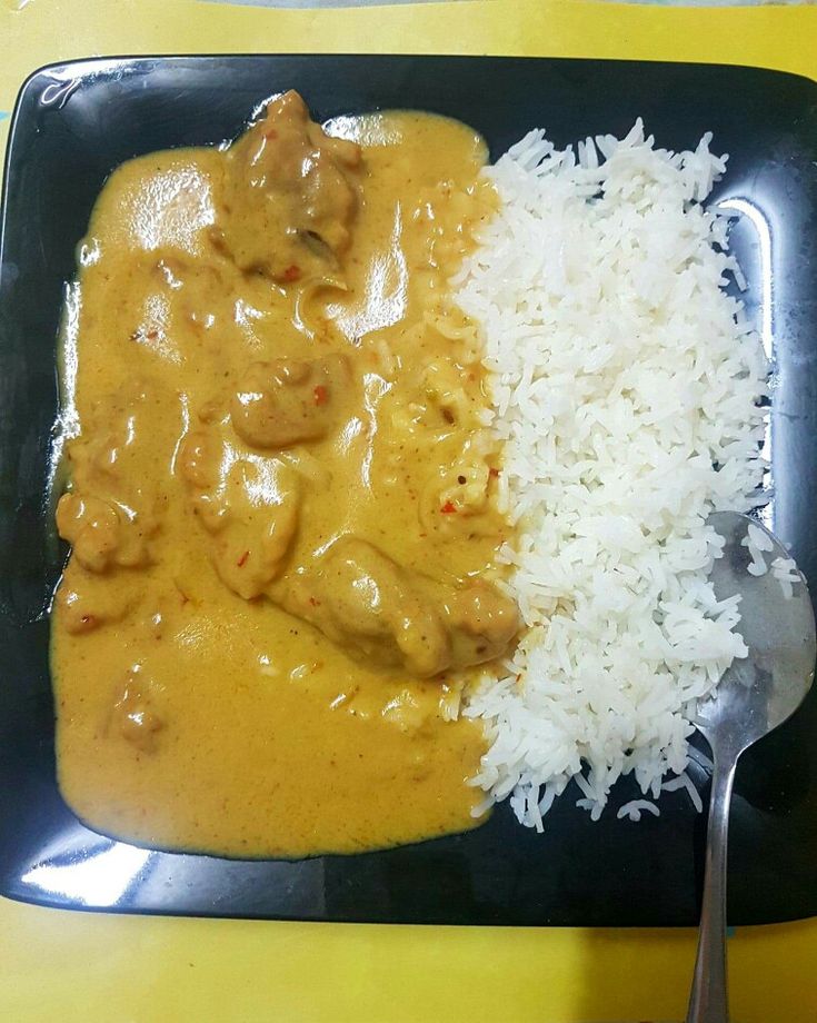 a black plate topped with rice and meat covered in gravy