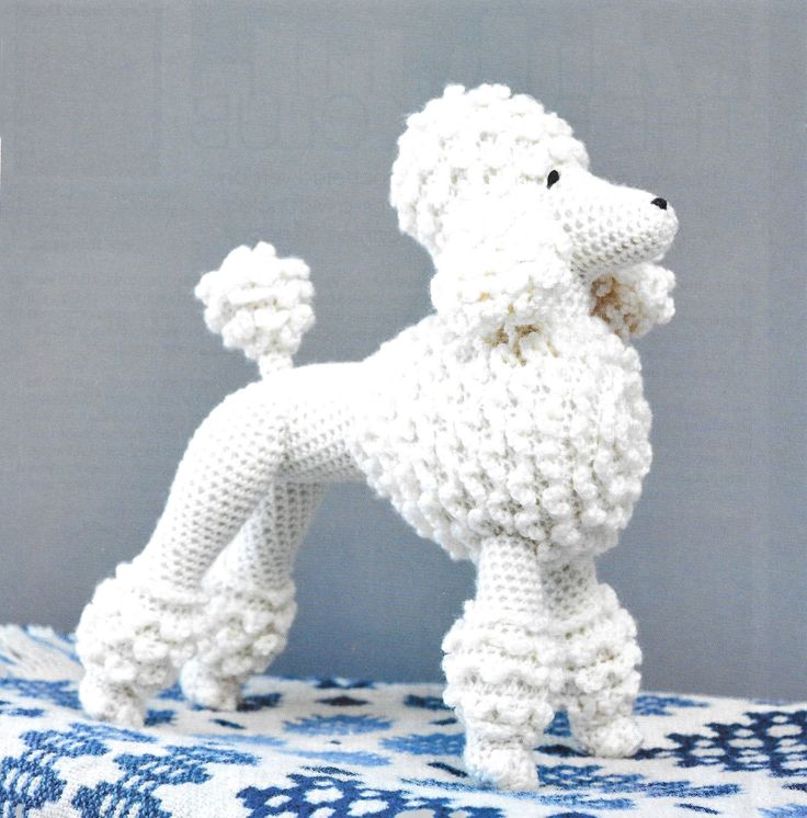 a knitted poodle sitting on top of a blue and white tablecloth covered surface