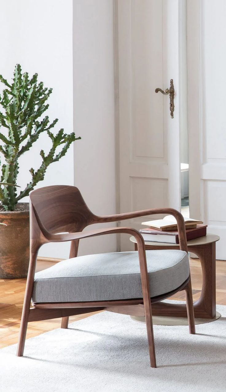 a wooden chair sitting on top of a white rug next to a potted plant