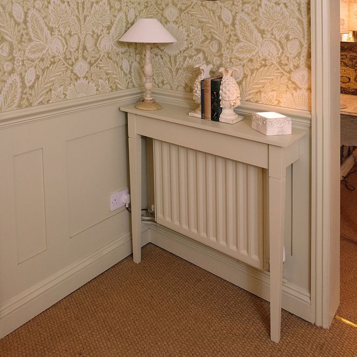 a white table with a lamp on top of it next to a wallpapered wall