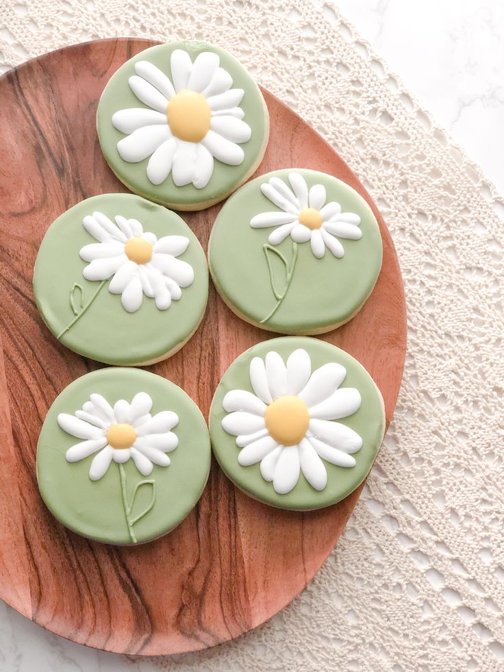 four cookies decorated with green icing and white daisies on a wooden platter