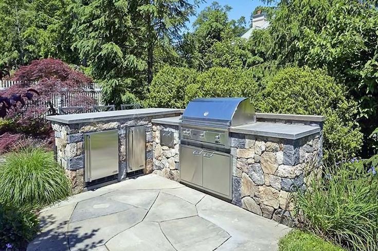 an outdoor kitchen with stone walls and grilling area in the middle of some trees