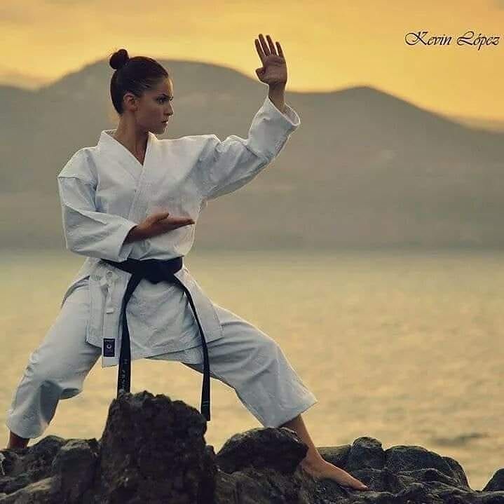 a woman is practicing karate on the rocks by the water at sunset or sunrise with her hands in the air