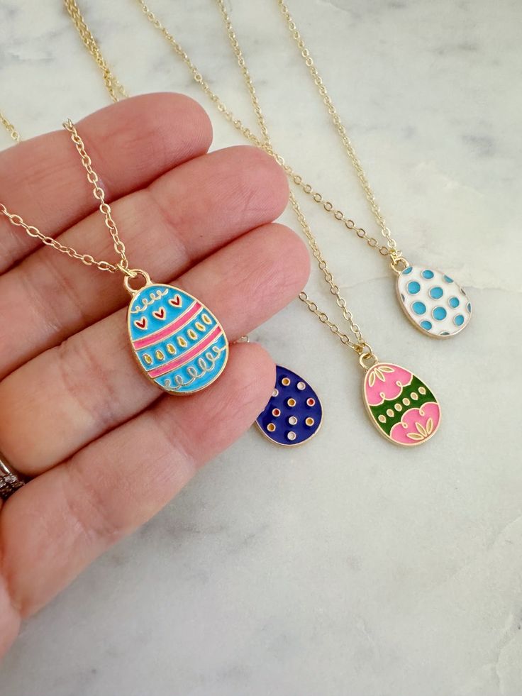 three necklaces in different colors and designs on a person's hand with gold chain