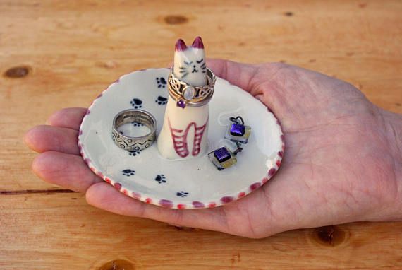 a hand holding a small ring dish with two cats on it and one cat in the middle