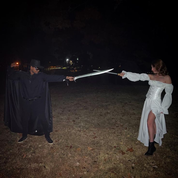 a man and woman dressed up as witches holding swords in their hands at night time