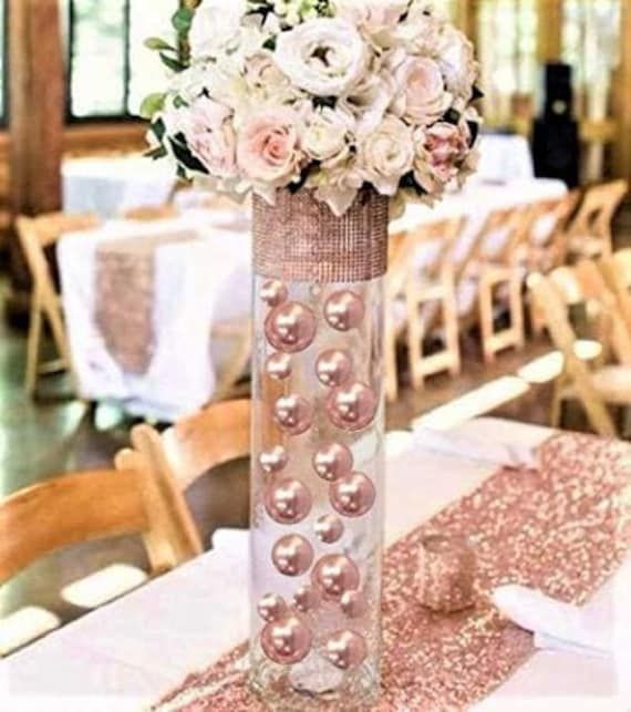 a tall vase filled with white flowers on top of a table covered in pink sequins