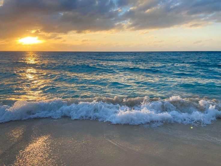 the sun is setting over the ocean with waves crashing on the sand and blue water