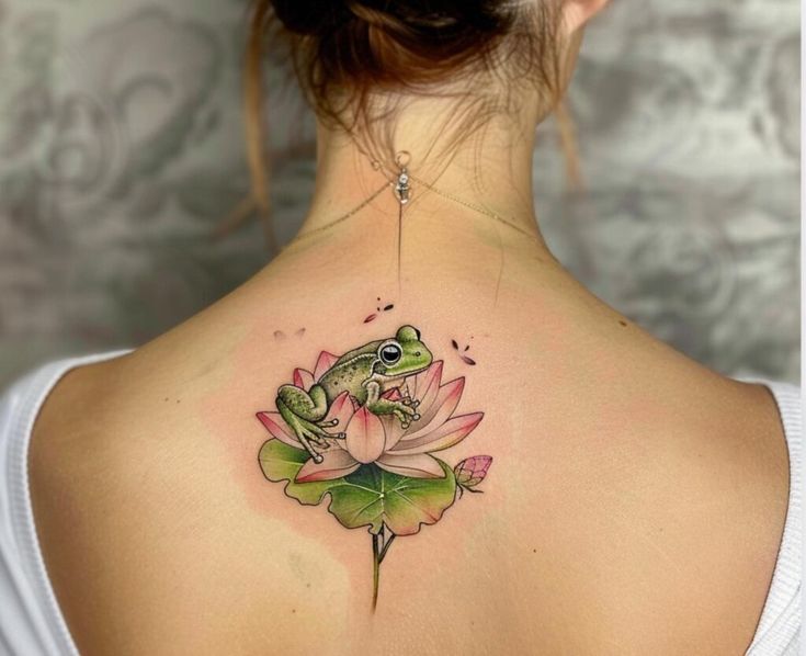 a woman's back with a frog and lily flower tattoo on her left shoulder