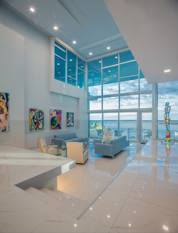 a living room with white walls and flooring next to large windows overlooking the ocean