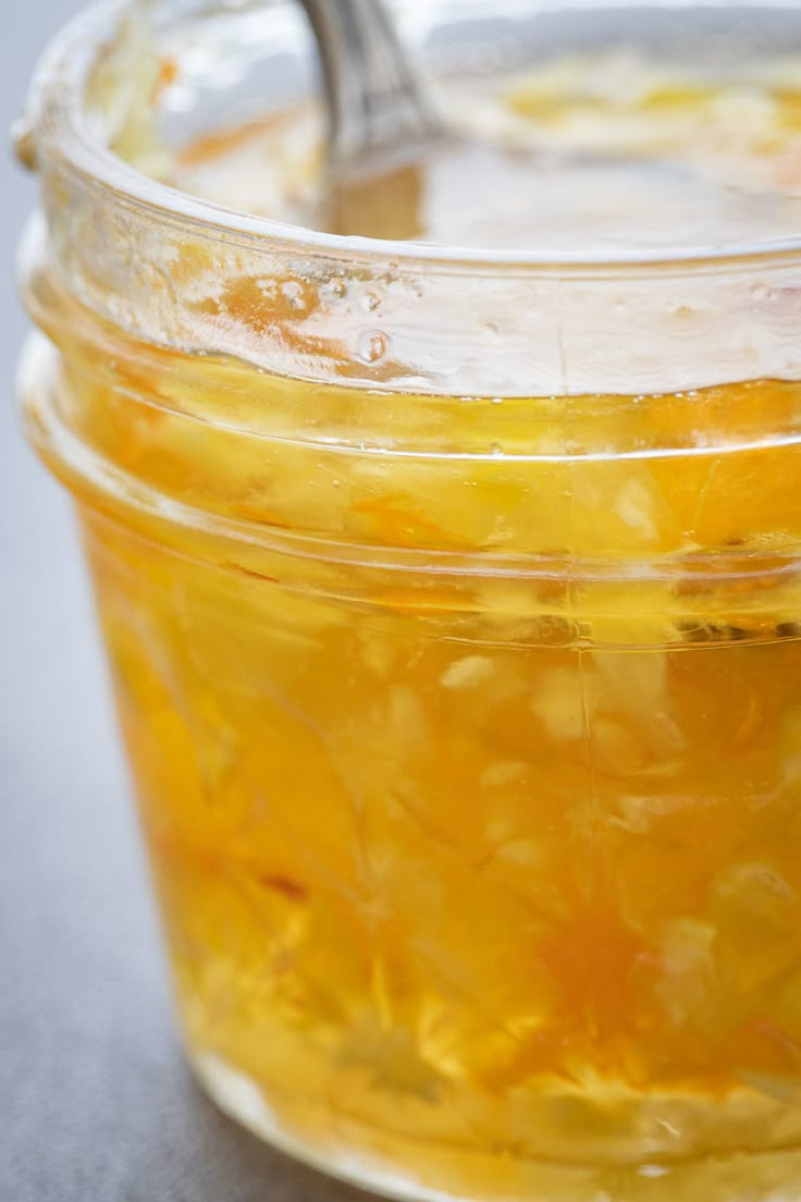 a jar filled with yellow liquid sitting on top of a gray table next to a spoon