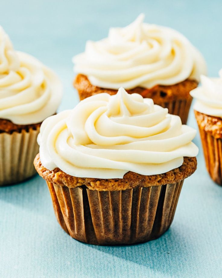 three cupcakes with white frosting sitting on top of a blue tablecloth