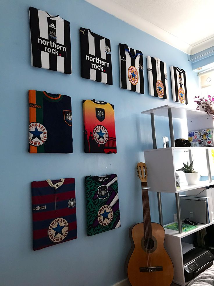 a guitar is sitting in front of several soccer jerseys on the wall