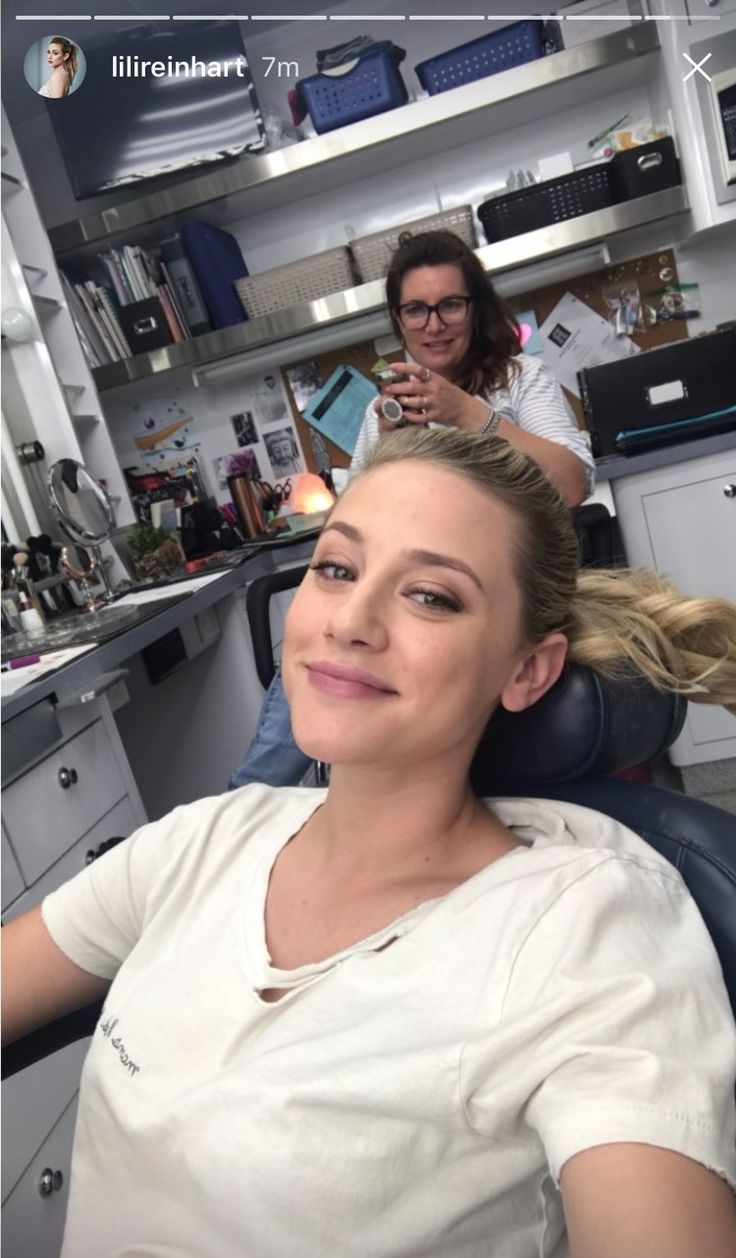 a woman sitting in a hair salon chair with another person behind her looking at the camera