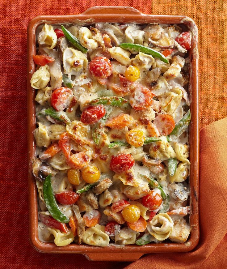 a casserole dish with tomatoes, pasta and spinach in it on an orange cloth