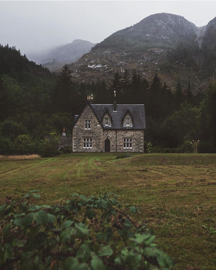 an old stone house in the middle of a field with mountains in the back ground