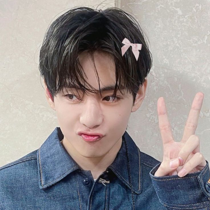 a young man making the peace sign with his hand and wearing a denim shirt on