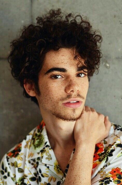 a young man with curly hair wearing a flowered shirt and looking at the camera